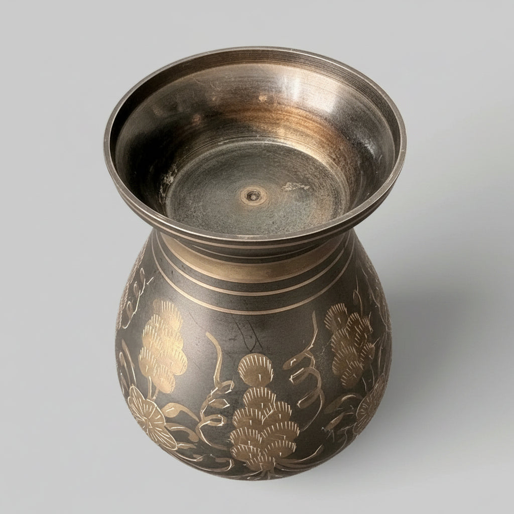 Bottom view of a vintage brass vase with light patina, etched with floral patterns on a grey background
