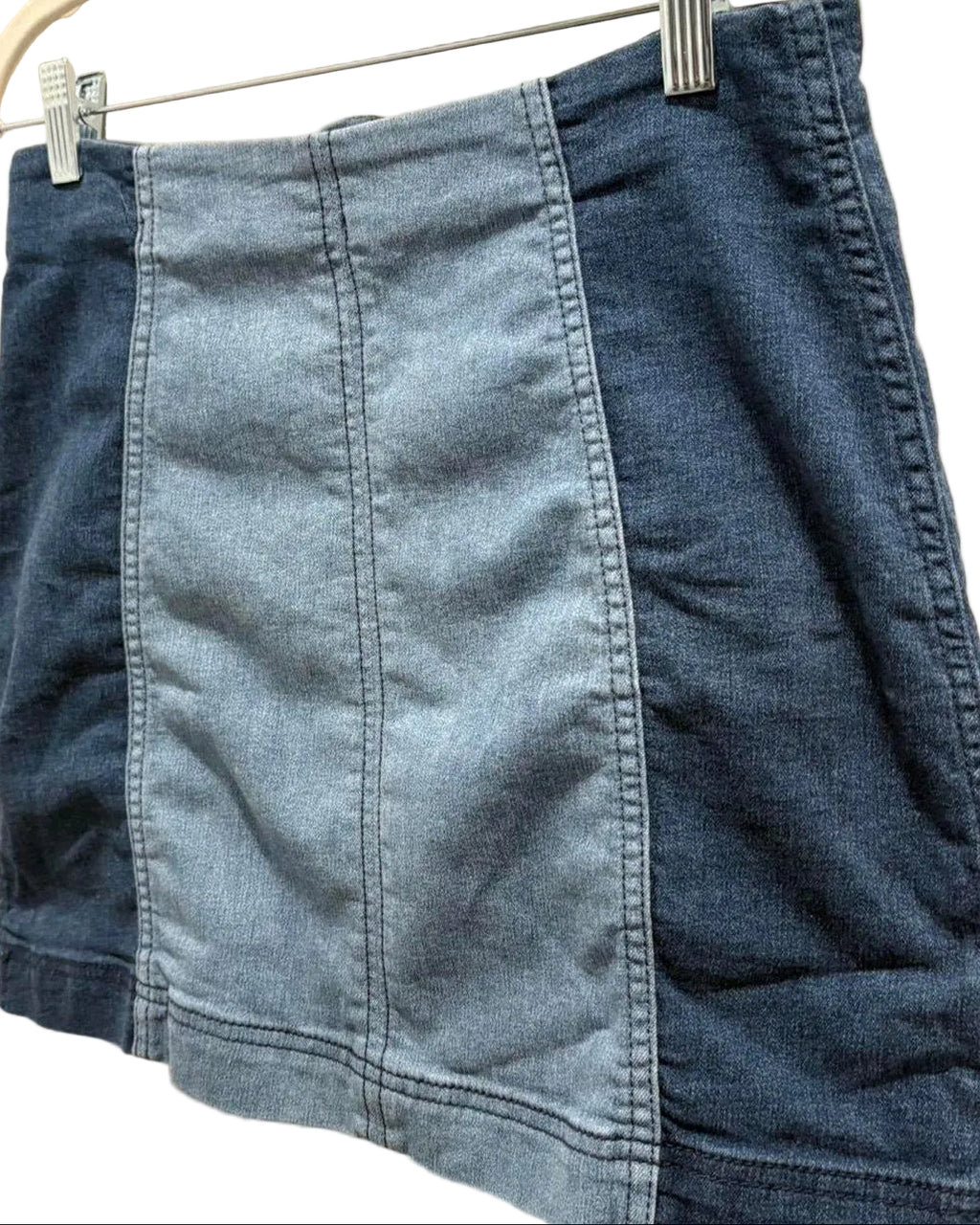 Blue two-tone denim mini skirt hanging on a white wall