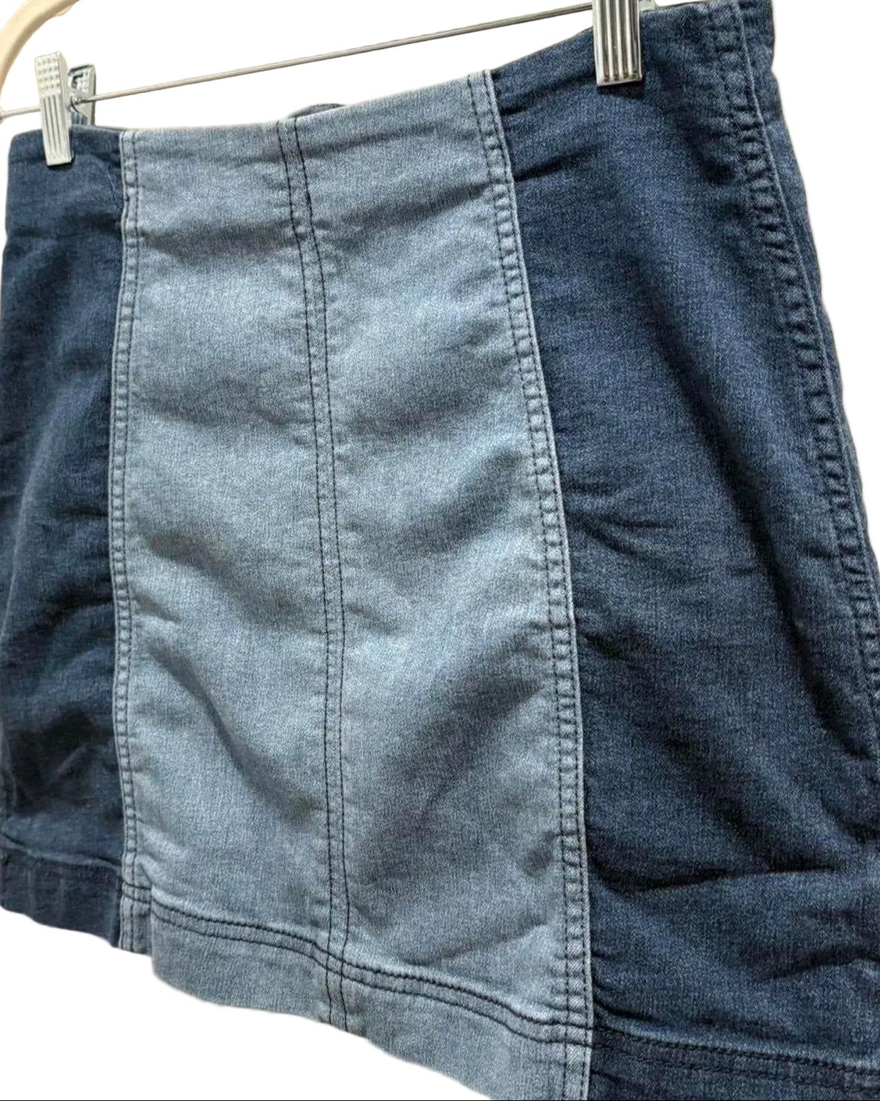 Blue two-tone denim mini skirt hanging on a white wall