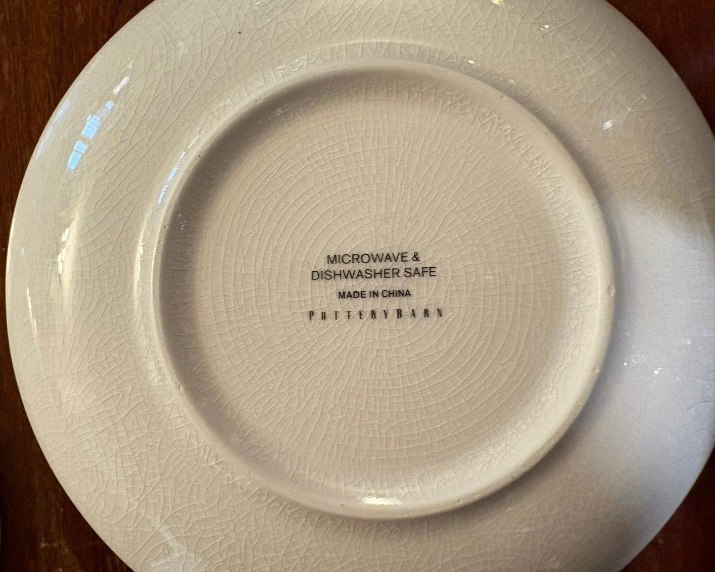 White ceramic plate with crazing, and 'POTTERYBARN' branding and safety information on a wooden surface.