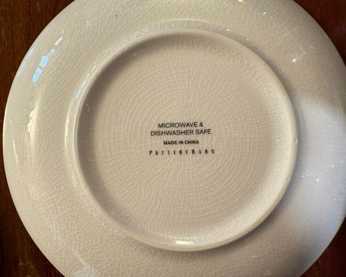 White ceramic plate with crazing, and 'POTTERYBARN' branding and safety information on a wooden surface.