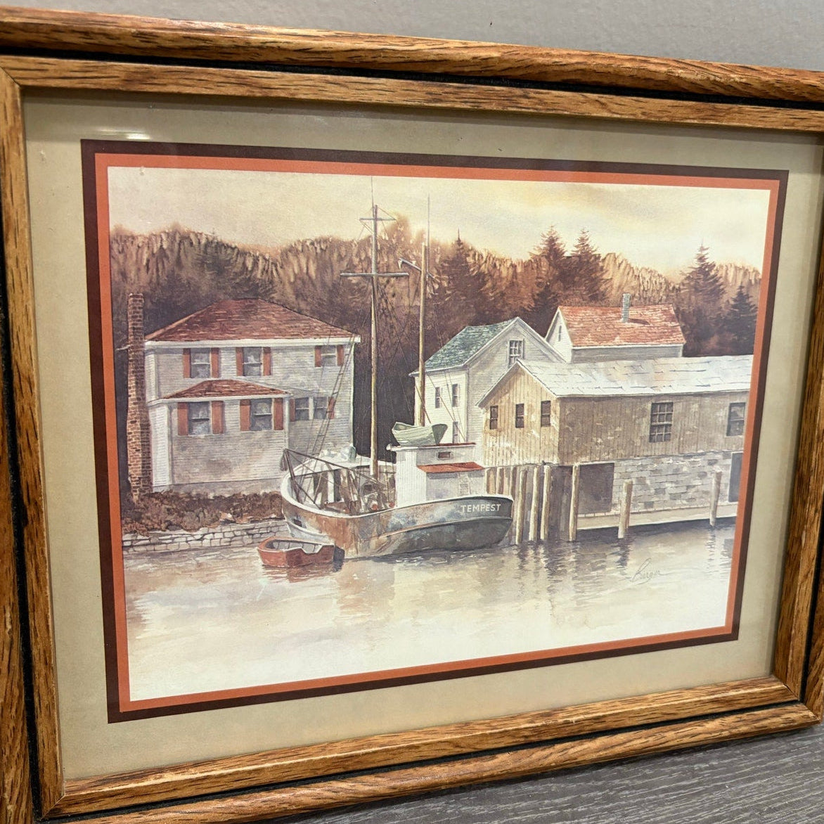 Framed painting of a coastal scene with houses and a boat.