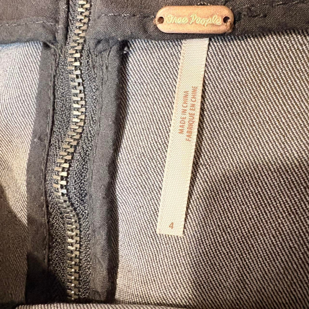 Close-up of a dark denim fabric with a zipper and a label on a product, featuring the brand 'Free People'.