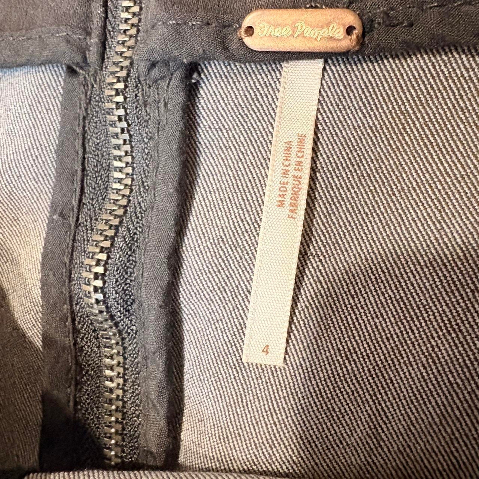 Close-up of a dark denim fabric with a zipper and a label on a product, featuring the brand 'Free People'.