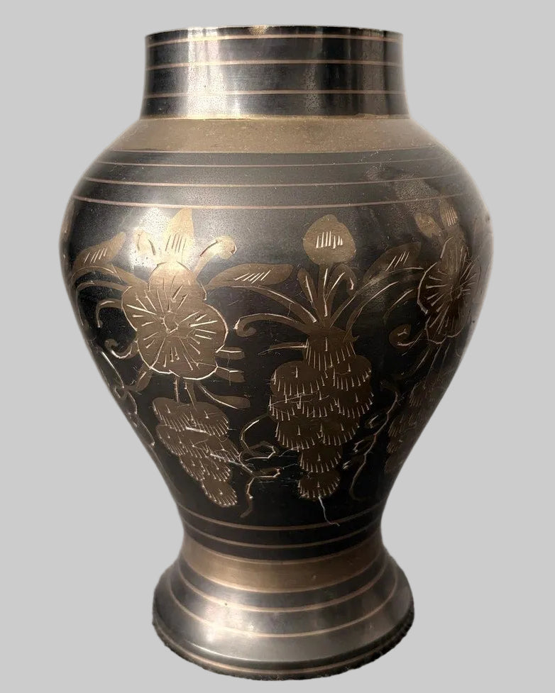 Close up of a decorative, vintage brass vase, etched with floral patterns, on a grey background