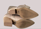 Bottom soles of a pair of lightly worn, taupe suede boots on a neutral background