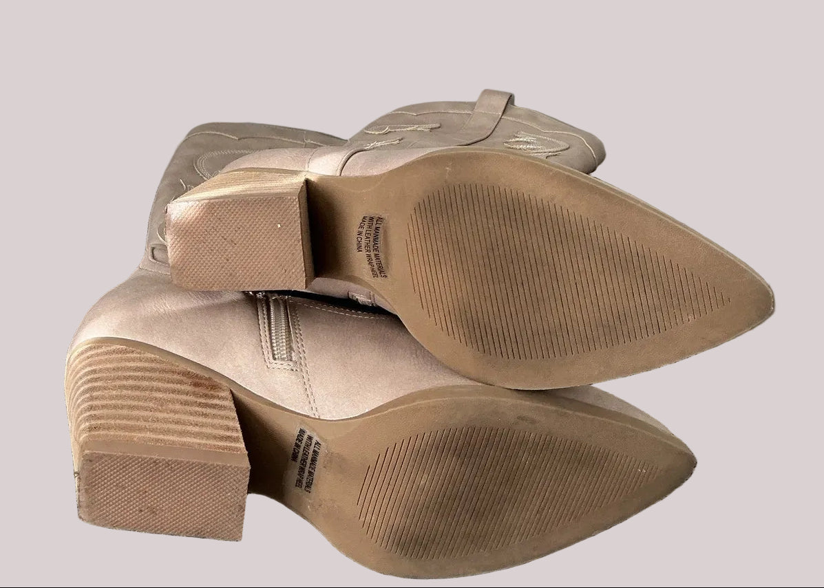 Bottom soles of a pair of lightly worn, taupe suede boots on a neutral background