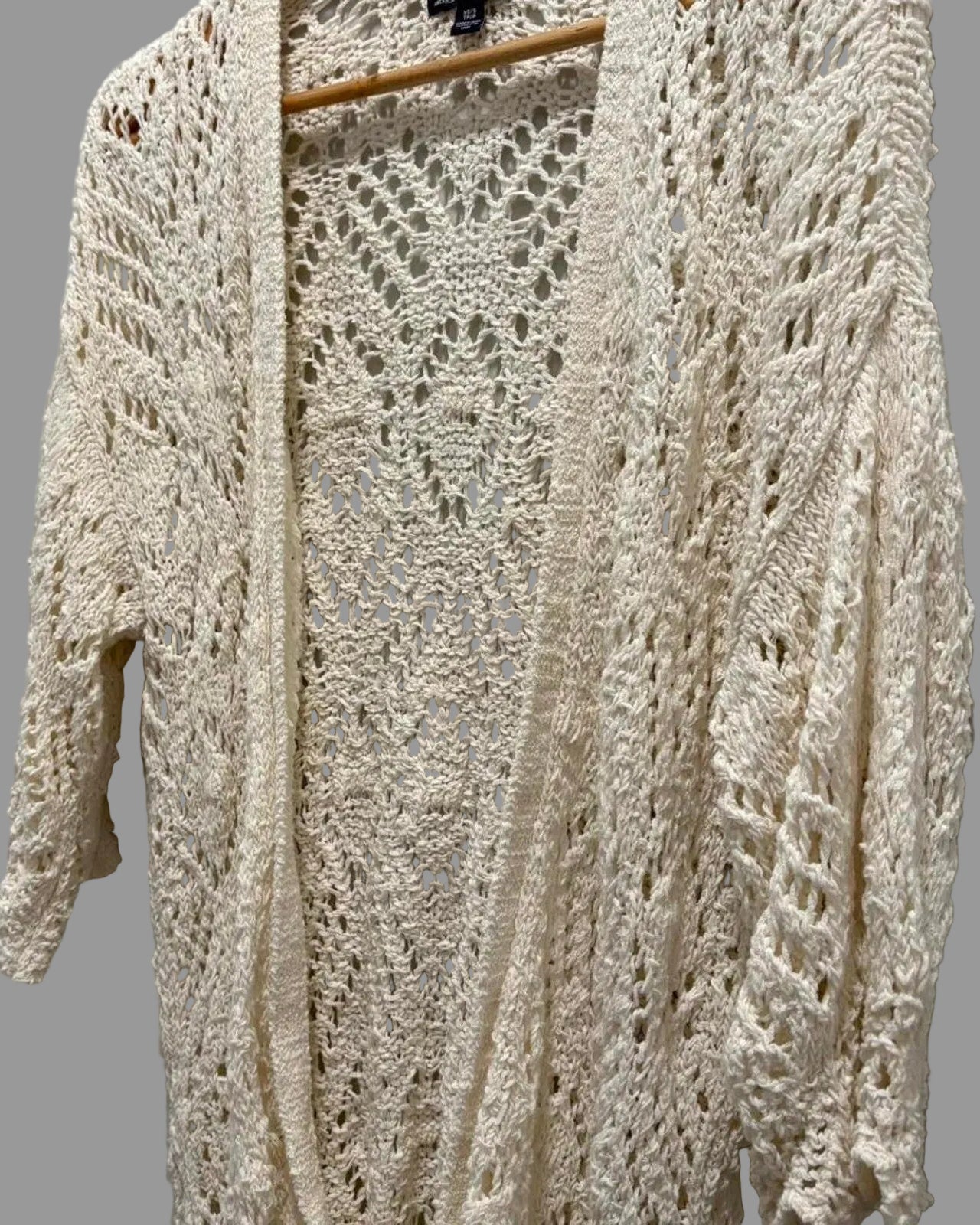 Cream crochet cardigan on a hanger against a plain background