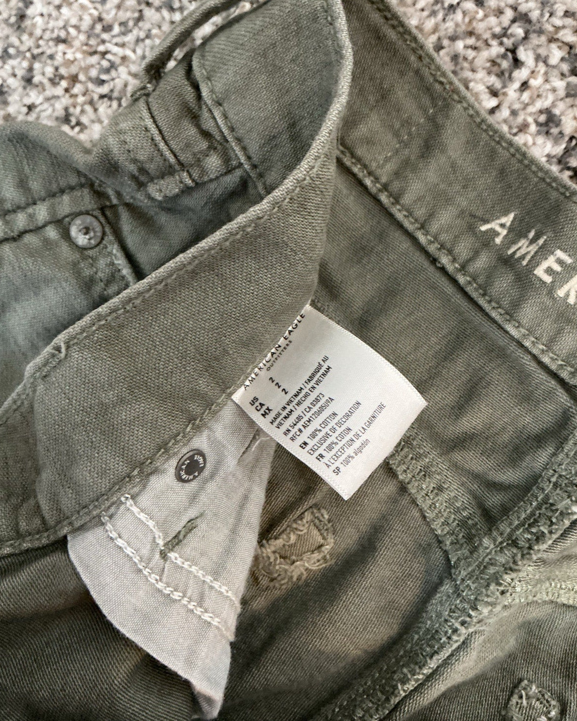 Folded green pants with a tag on a textured surface
