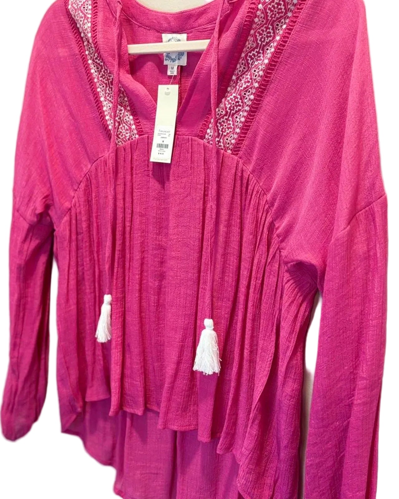 Pink long-sleeve boho top with tassel details on a white background