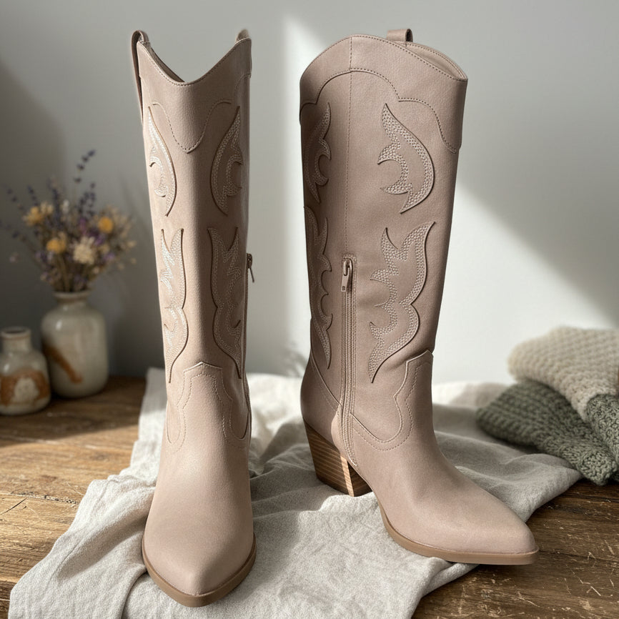Cottagecore aesthetic, pair of taupe western cowboy boots on a textured surface with a neutral floral background.