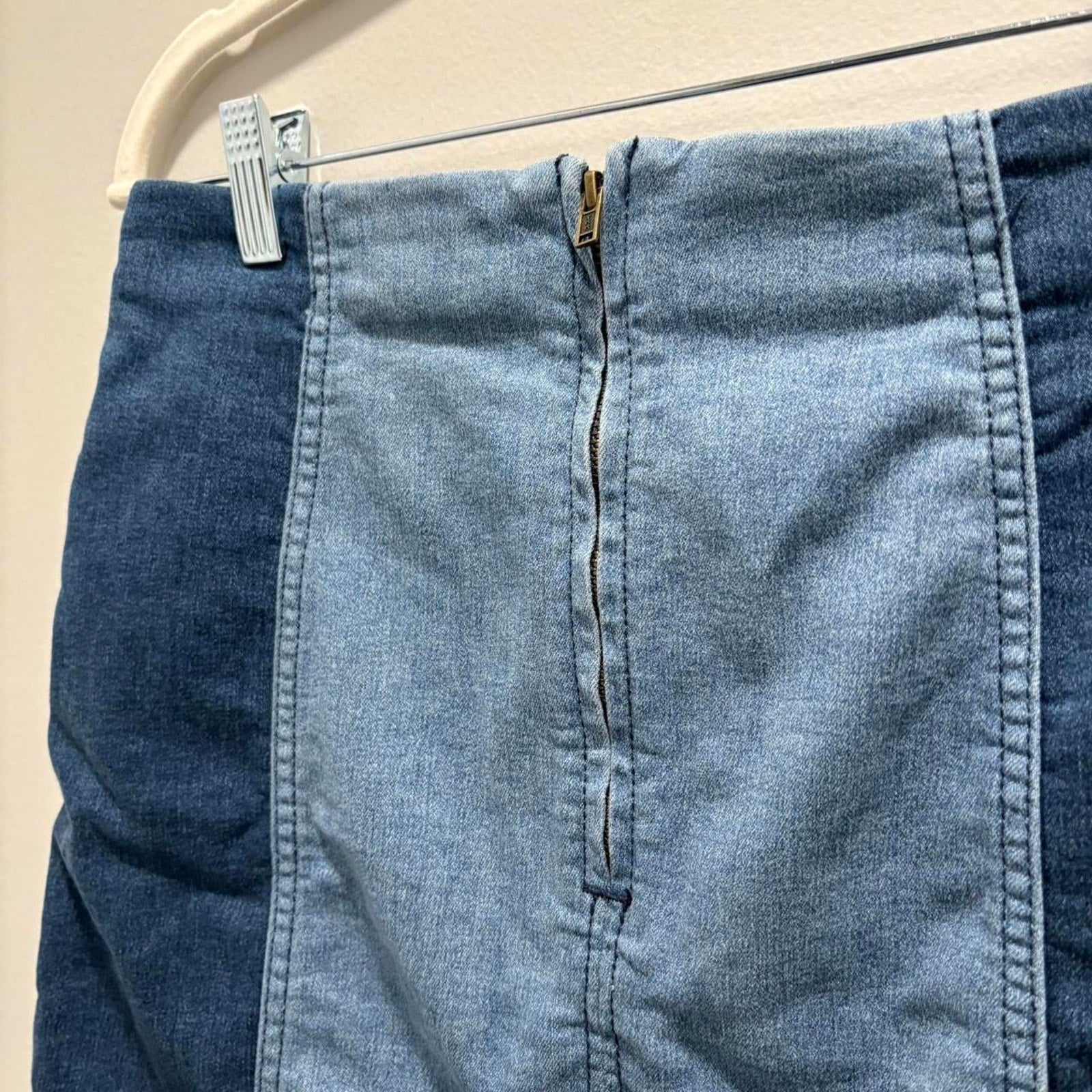 Denim mini skirt with zip back hanging on a beige wall.