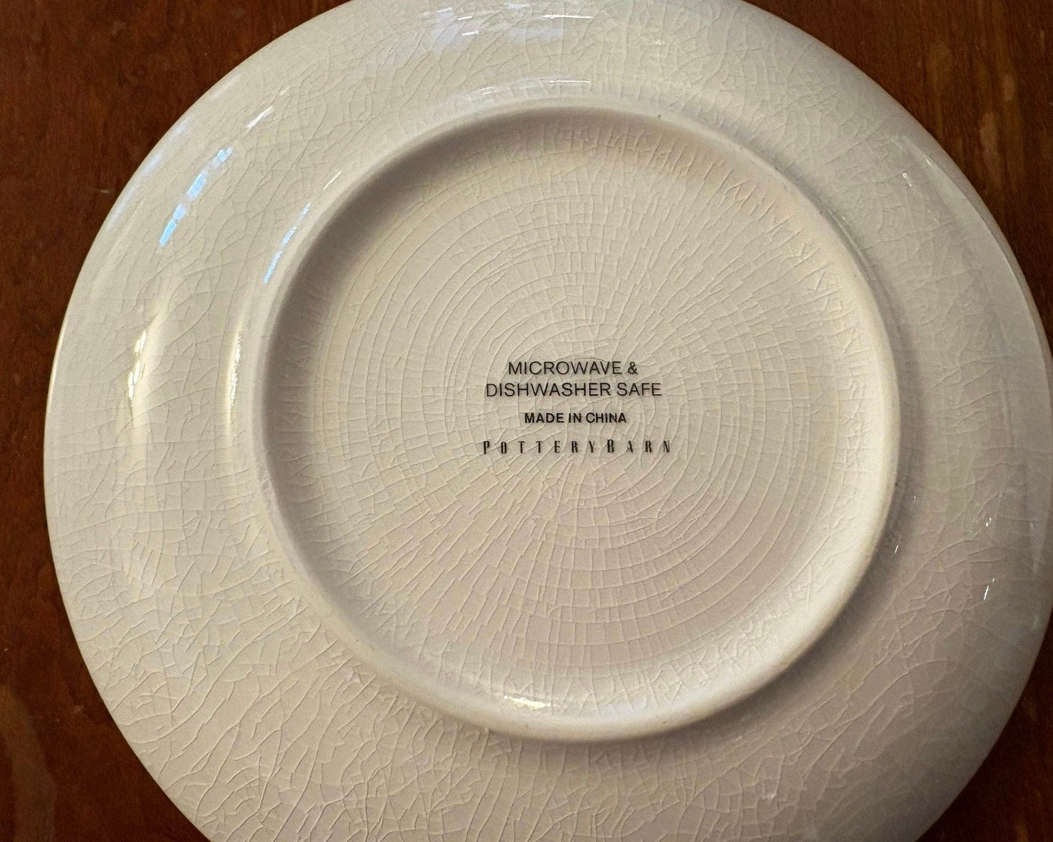White ceramic Pottery Barn small plate with crazing crackled glaze, and 'Microwave & Dishwasher Safe' text on a wooden surface