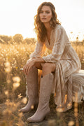 A bohemian aesthetic photo of a model wearing a pair of taupe cowboy boots in a field.
