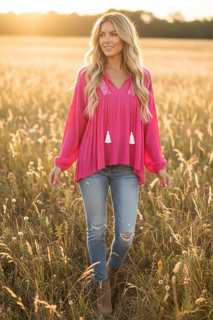 Pink long-sleeve boho top with embroidered decorative elements on a model in a field