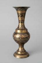 Sunlight hitting a decorative brass vase etched with intricate patterns on a grey surface.