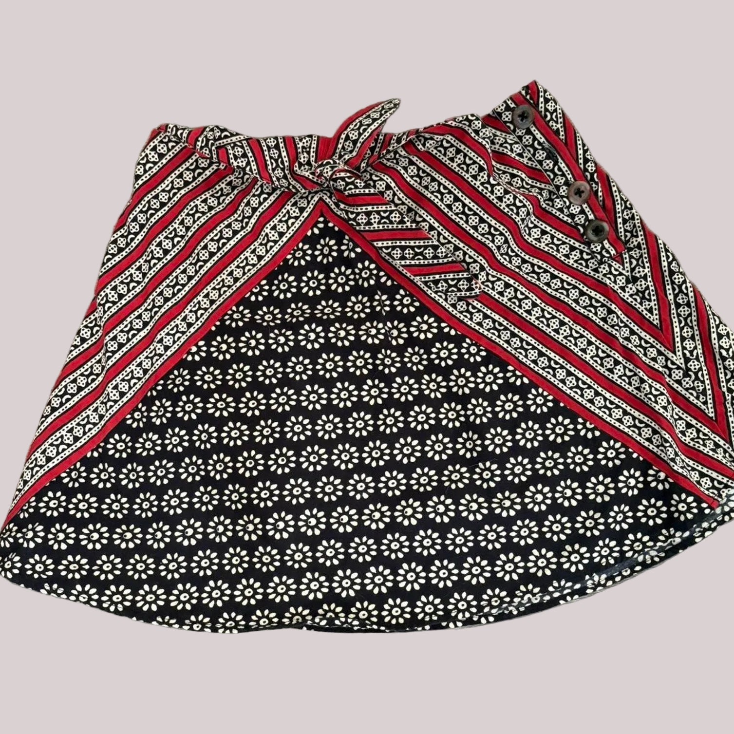 Mini fabric skirt with red, white, and black patterns and tie front on a white background