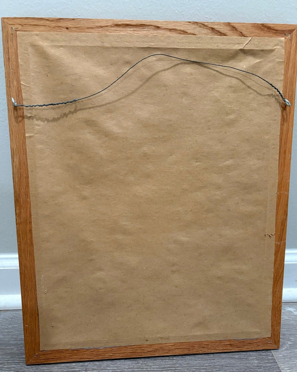Wooden picture frame with a brown mat and hanging wire on a light gray background