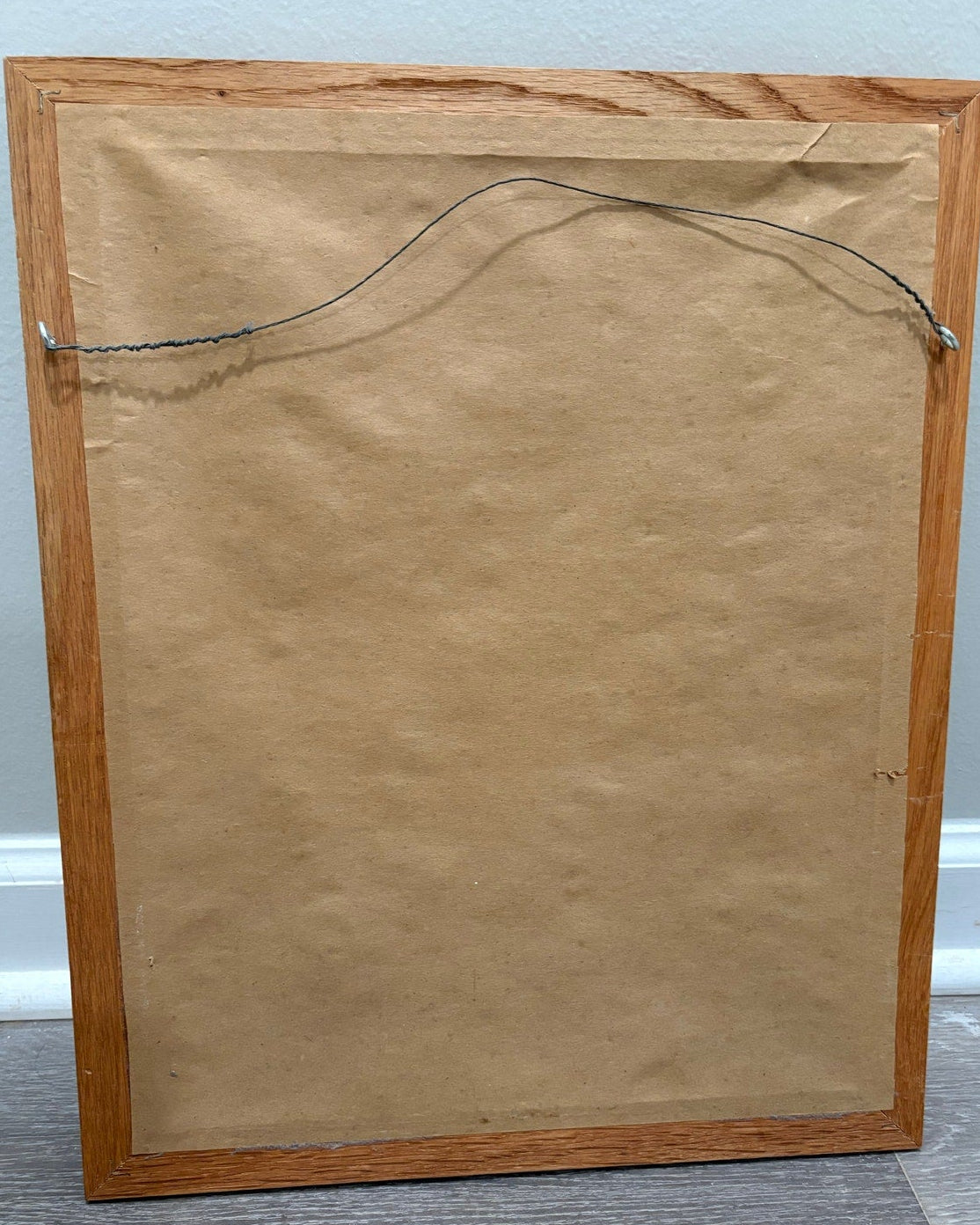 Wooden picture frame with a brown mat and hanging wire on a light gray background
