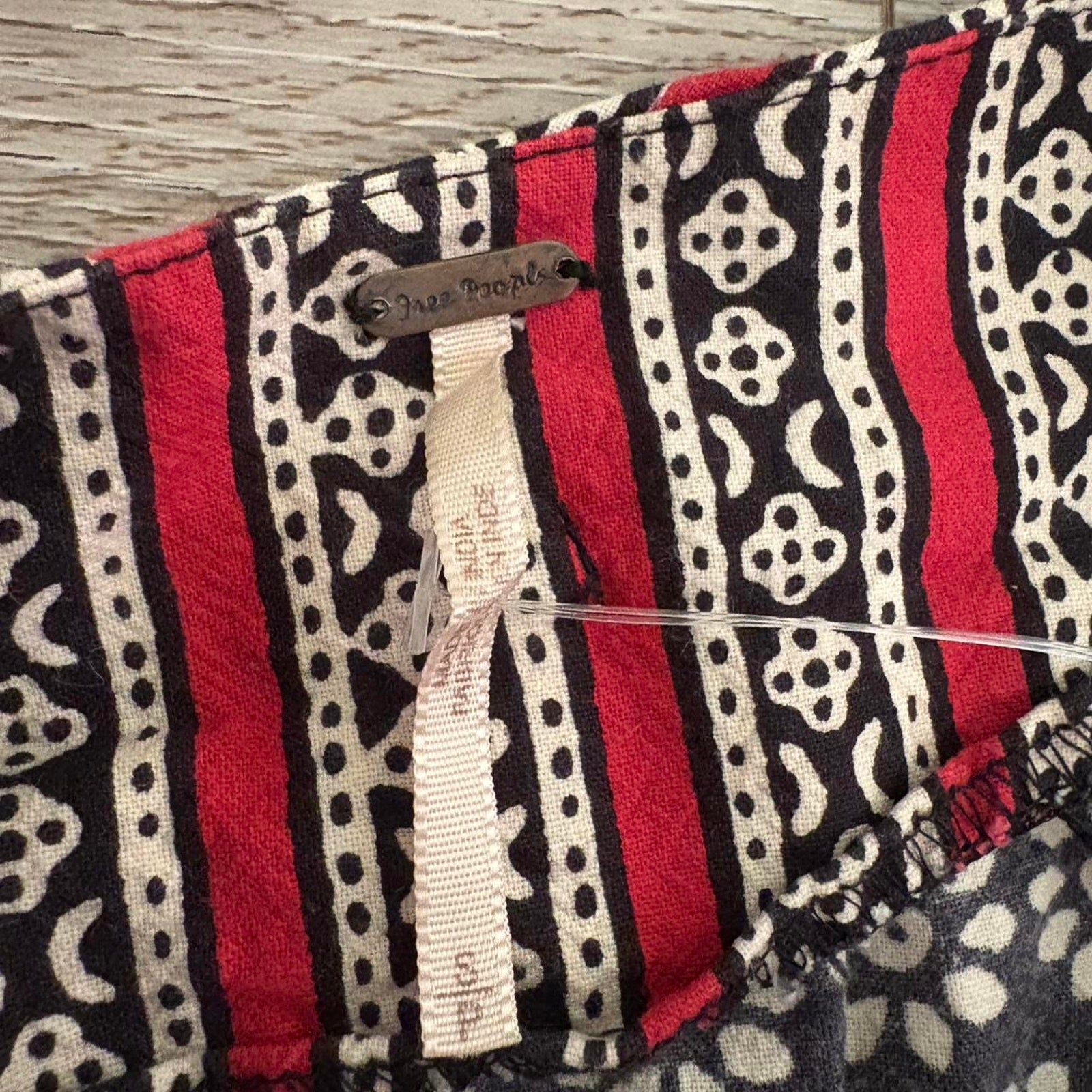 Close-up of a fabric skirt with red, black, and white pattern tagged "Free People" brand.