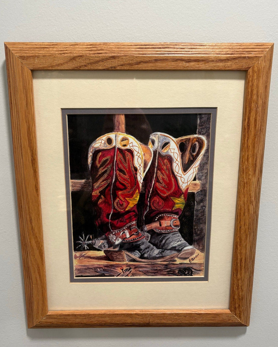 Framed artwork of red cowboy boots with a wooden frame on a gray wall.