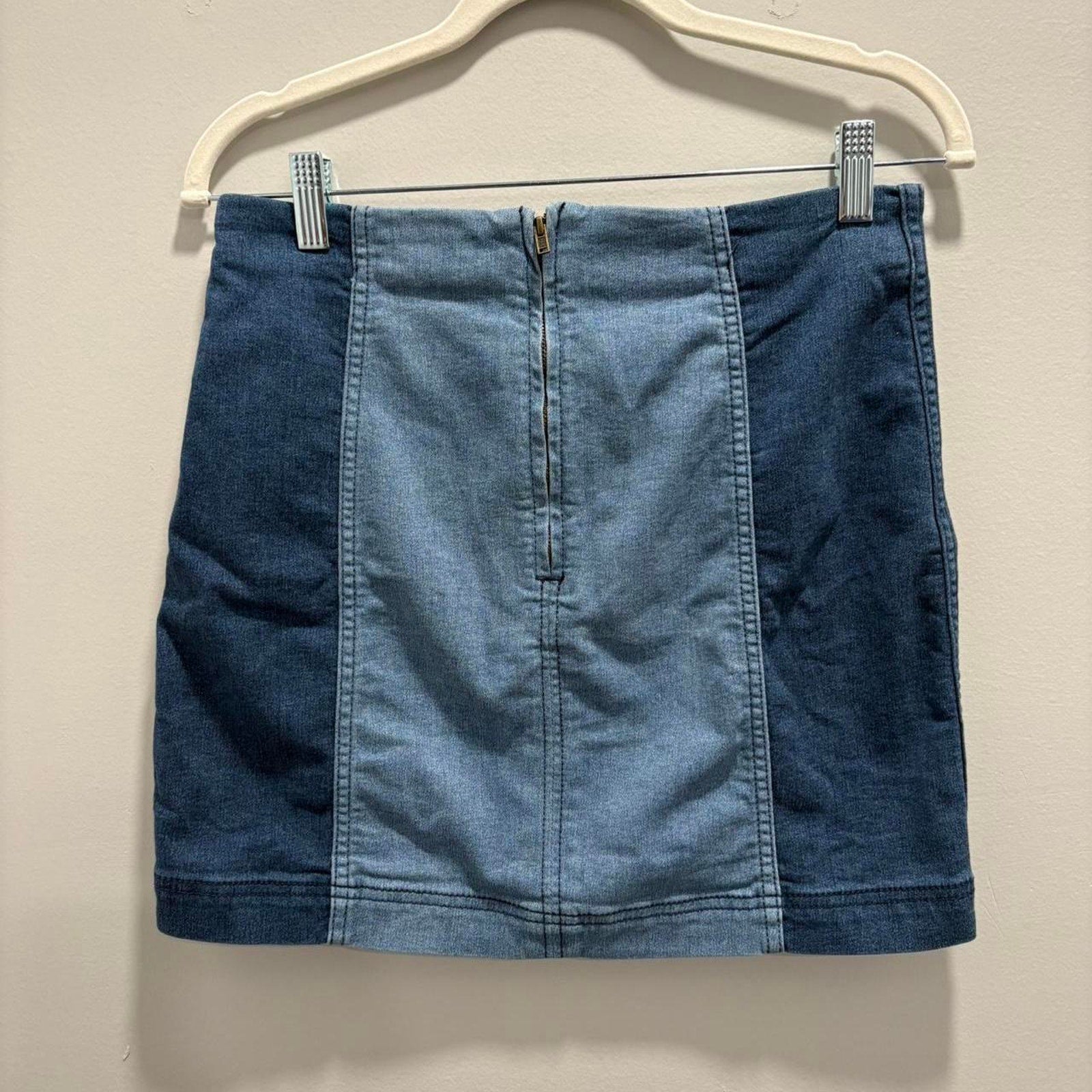 Blue denim skirt on a hanger against a beige background