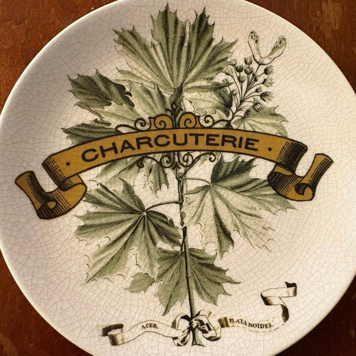 Decorative Pottery Barn plate with leaf design and 'Charcuterie' text on a wooden surface