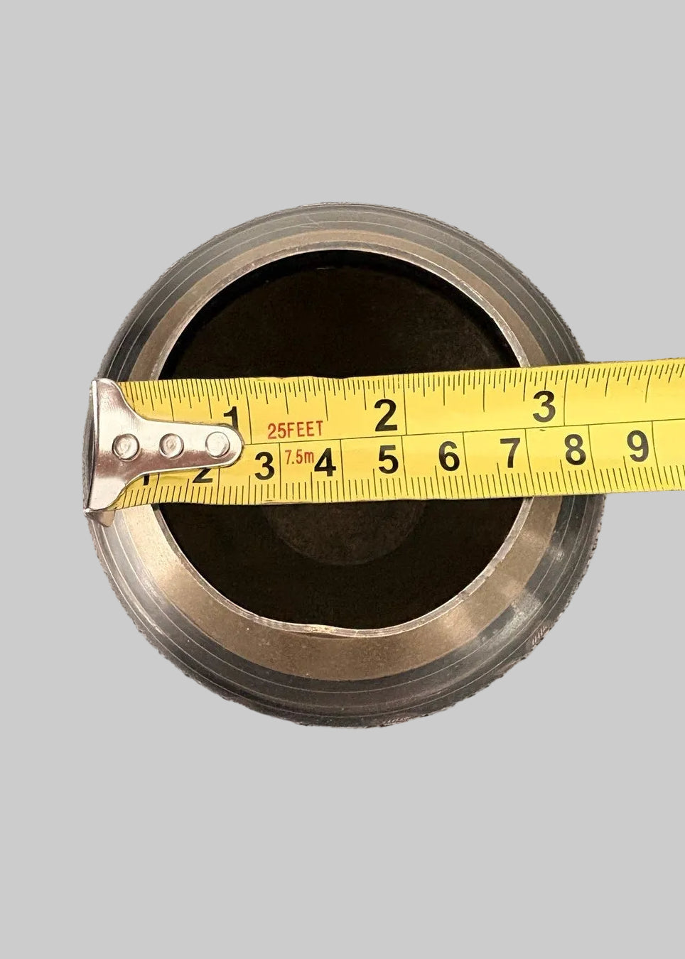 Measurement of the opening of a vintage brass vase, measuring approximately 3" wide, on a grey background.