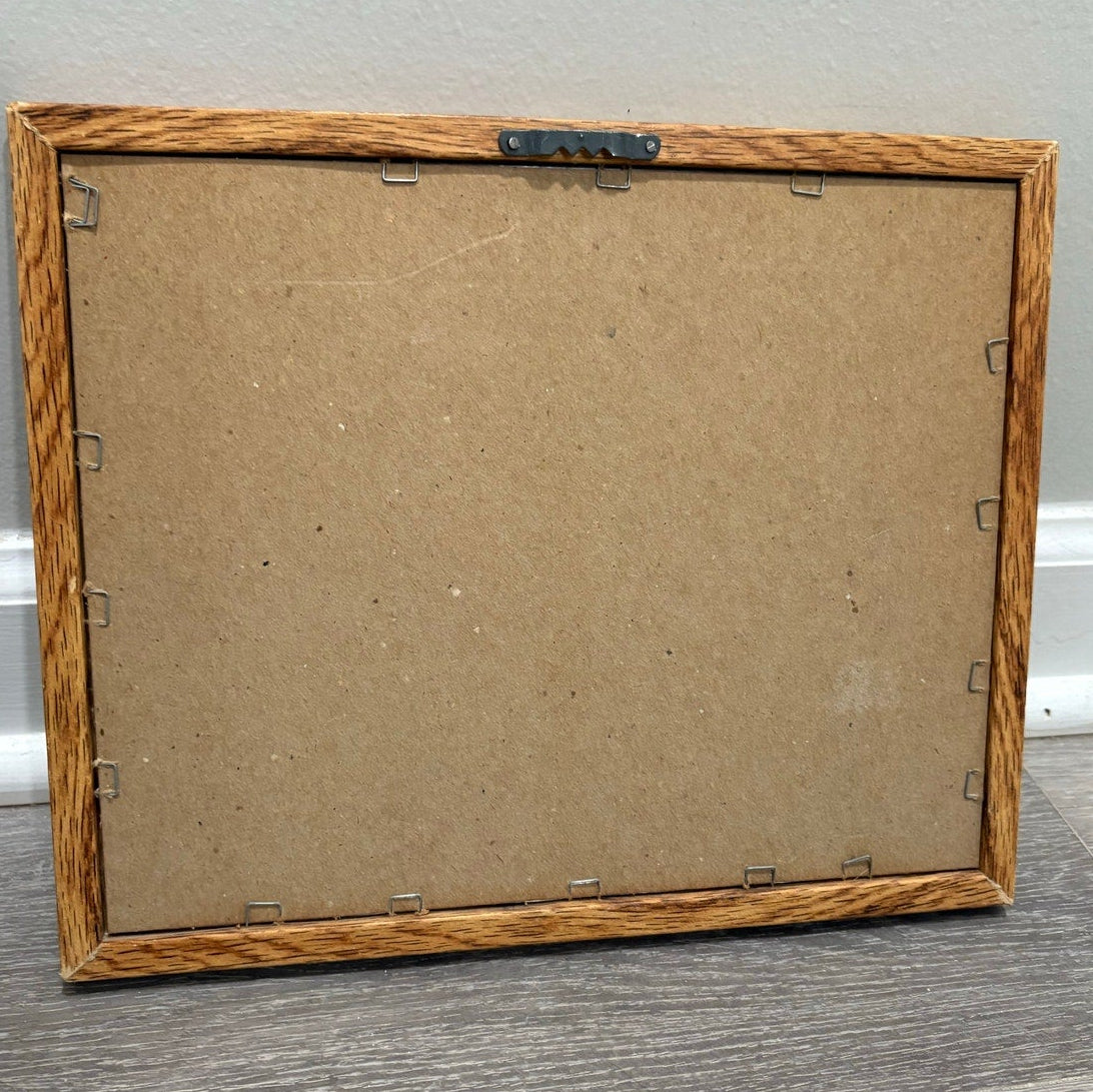 Back of a wooden picture frame with wall hook on a gray background.
